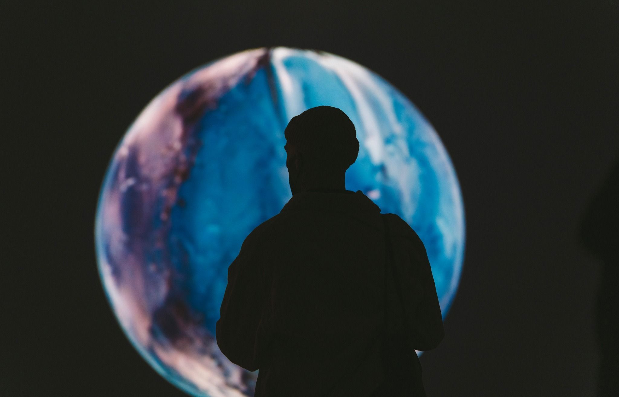 Photograph from the Distinct art exhibition. Background is black with a blue and purple sphere in the centre, and a person's sillhouette in front of the sphere